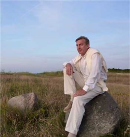 Portrætfoto af Niels Eje, som sidder på en sten ude i naturen og kigger ud i horisonten